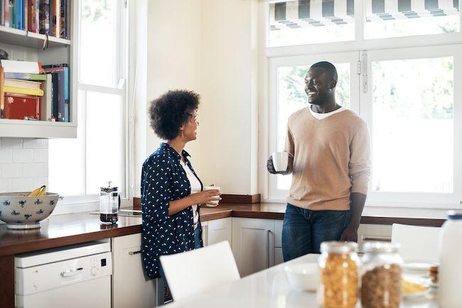 Couple standing in kitchen discussing something over coffee.